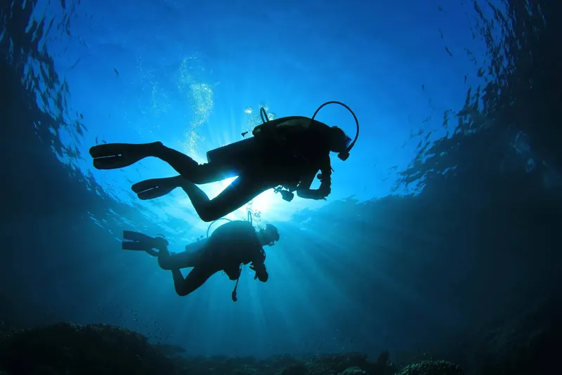 Deux plongeurs explorent les profondeurs bleues, lumière du soleil filtrant