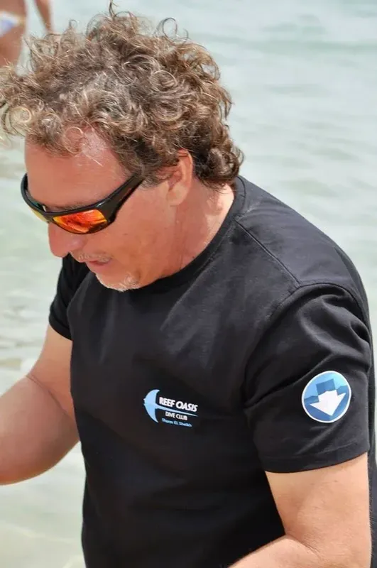 Homme portant des lunettes de soleil et un t-shirt noir sur une plage