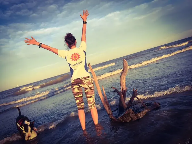 Femme bras levés sur une plage, vêtue d'un t-shirt avec un logo