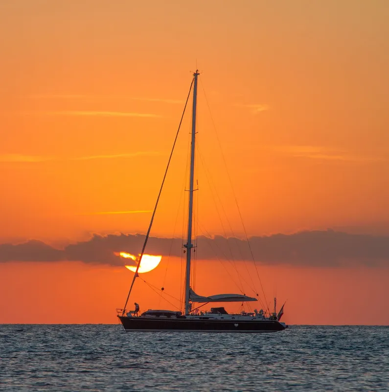 Voilier silhouette sombre sur mer au coucher du soleil orangé