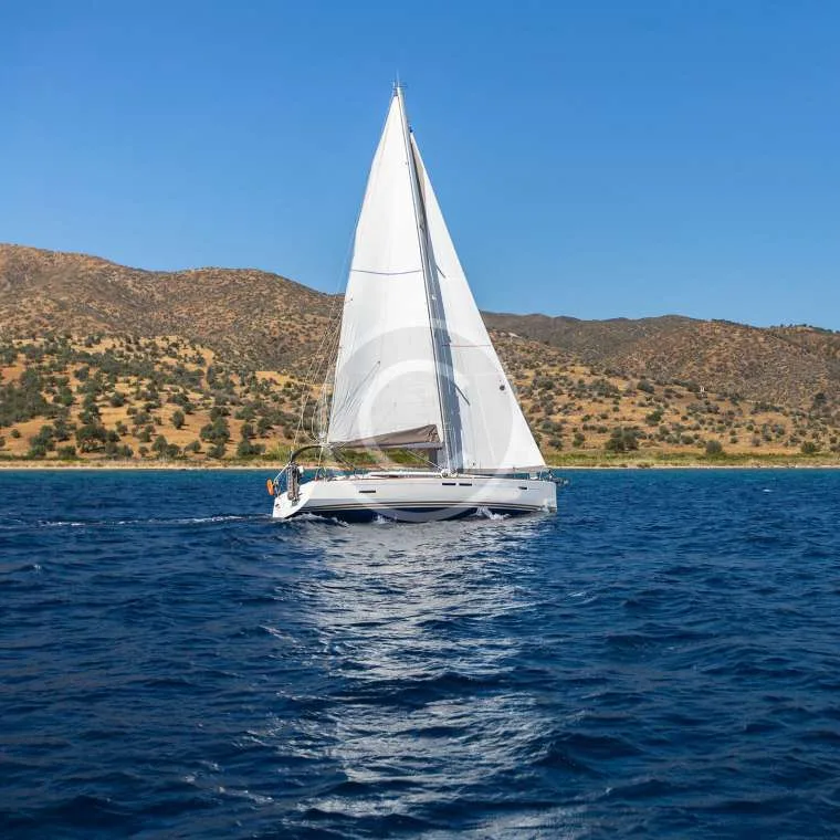 Voilier blanc naviguant sur une mer bleue avec des collines en arrière-plan