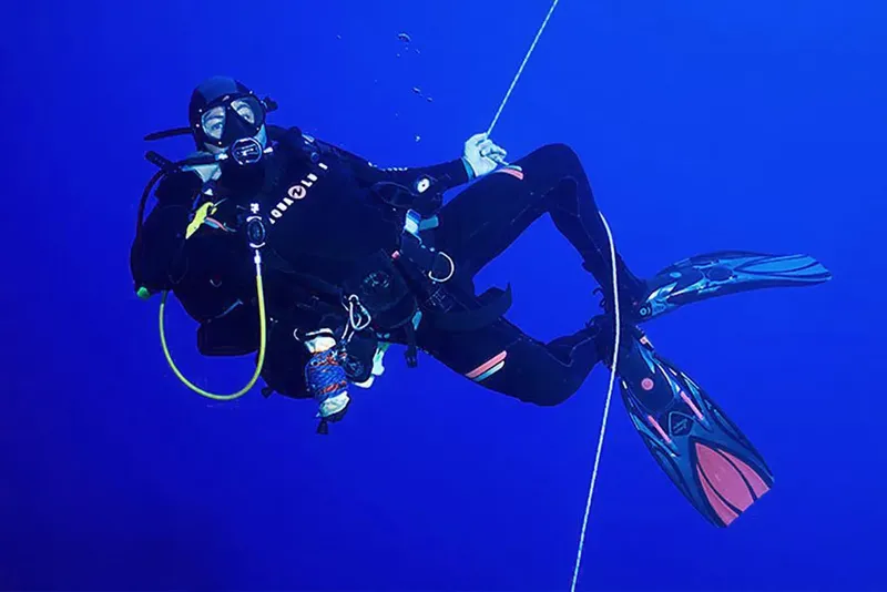 Plongeur en combinaison noire nageant dans une eau bleue profonde