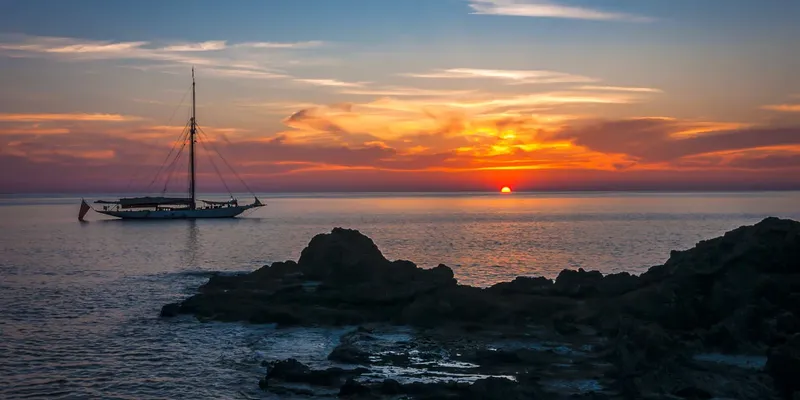 Voilier au coucher du soleil sur une mer calme et rocheuse