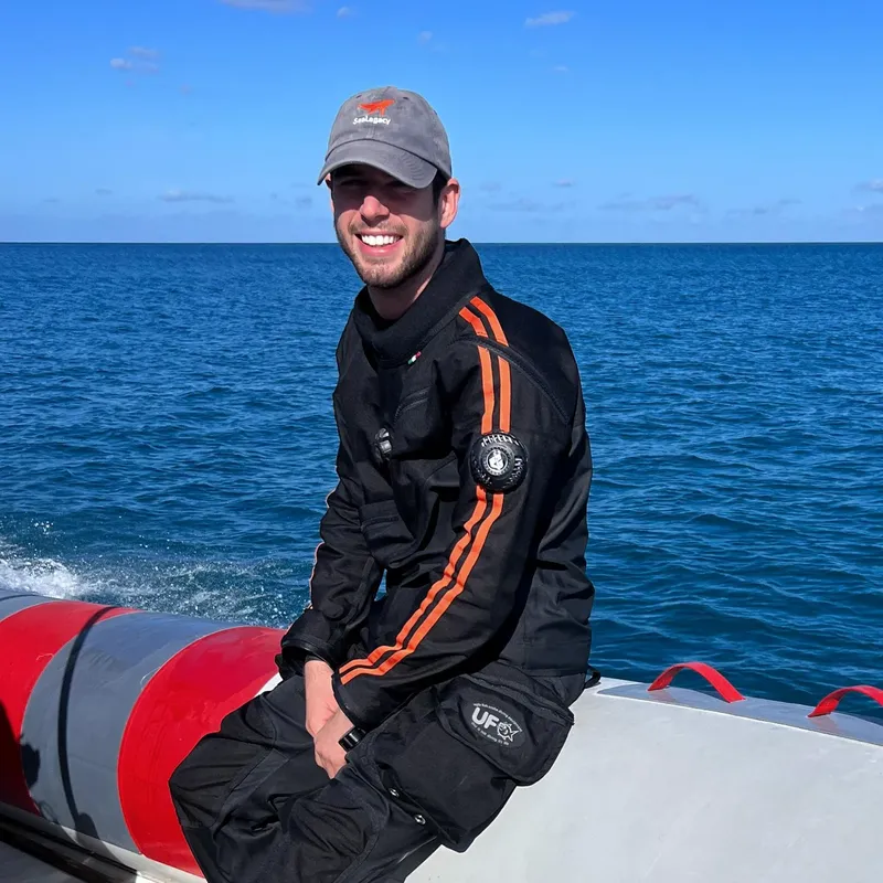 Un homme souriant porte une casquette et une combinaison noire sur un bateau
