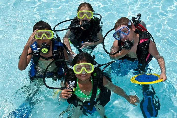 Quatre enfants sourient en équipement de plongée dans une piscine