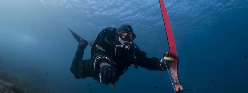 Plongeur en combinaison noire nageant avec un flotteur rouge en mer