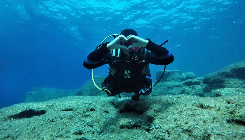 Plongeur en combinaison fait un cœur avec ses mains sous l'eau