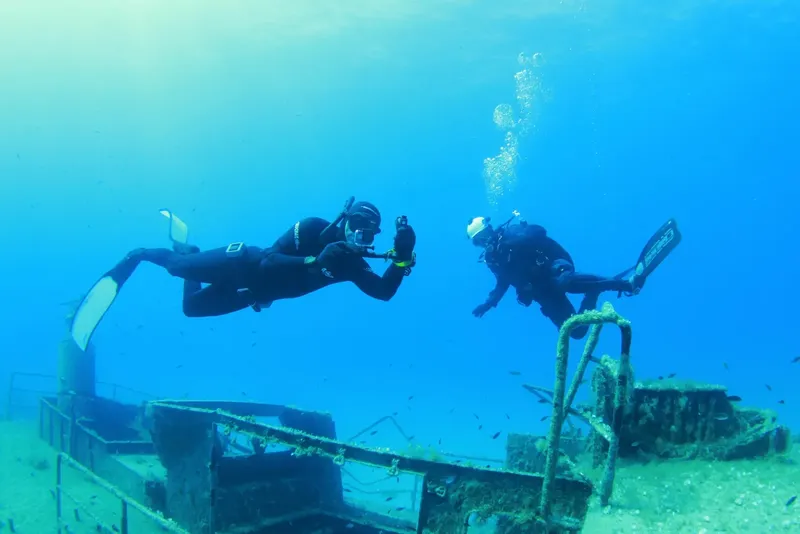 Deux plongeurs explorent une épave métallique sous l'eau bleue