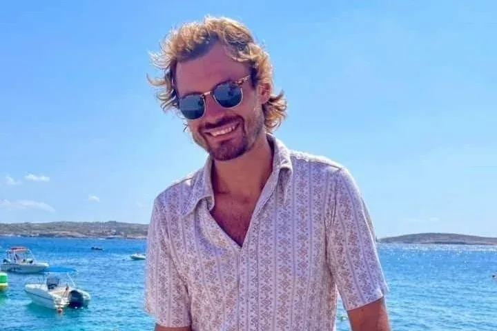 Homme souriant avec des lunettes de soleil devant la mer et bateaux