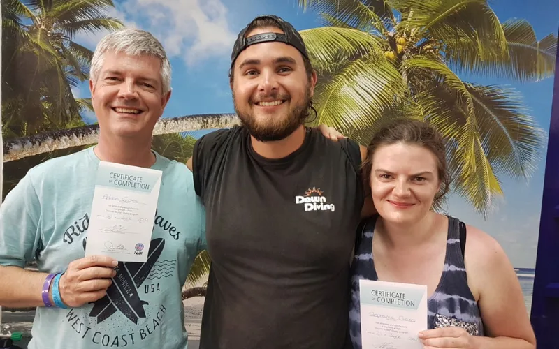 Trois personnes souriantes, deux tenant un certificat de plongée