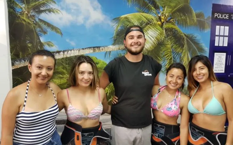 Cinq personnes souriantes posent devant un décor tropical et une cabine bleue