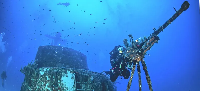 Plongeurs explorent une épave sous-marine avec des bancs de poissons