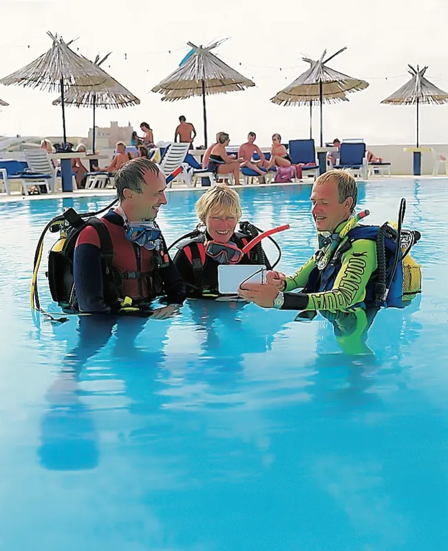 Trois plongeurs en formation dans une piscine ensoleillée discutent