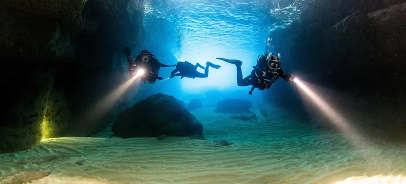 Trois plongeurs explorent une grotte sous-marine éclairée par leurs lampes