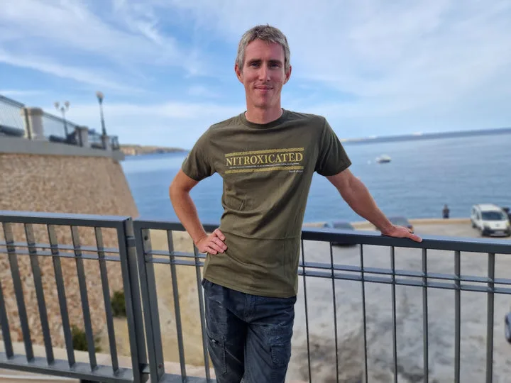 Un homme souriant se tient appuyé sur une rambarde en bord de mer