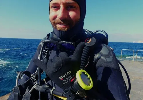 Plongeur en combinaison, équipé, souriant, face à la mer bleue
