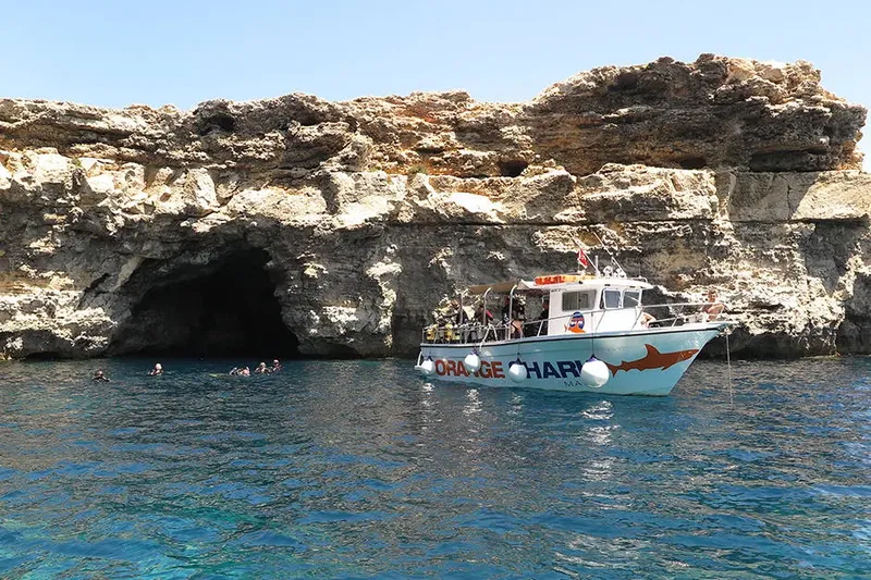 Bateau de plongée bleu et blanc près d'une falaise rocheuse et plongeurs