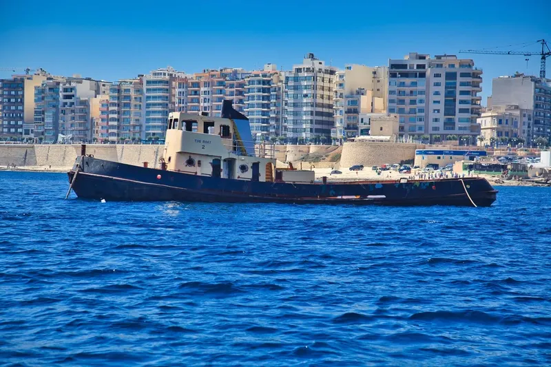 Bateau de pêche traditionnel amarré en mer, devant une ville côtière