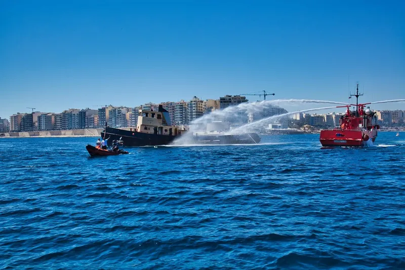 Plusieurs embarcations et un hélicoptère en mer, devant une ville
