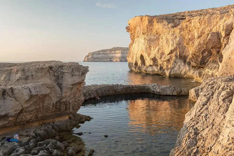 Personne assise sur des rochers au bord de l'eau turquoise
