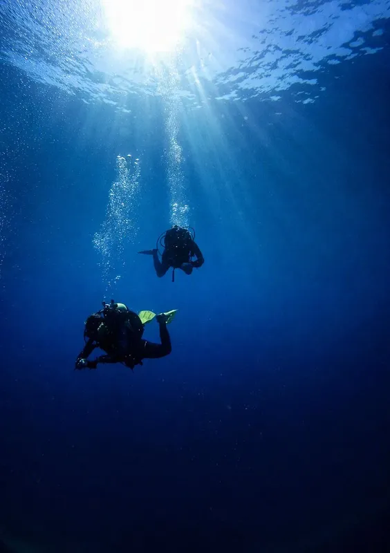 Deux plongeurs explorent les profondeurs bleues, lumière du soleil filtrant