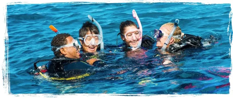 Quatre plongeurs souriants avec masque et tuba dans l'eau bleue