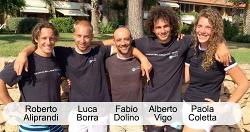 Cinq personnes souriantes posent ensemble devant un mur de pierres