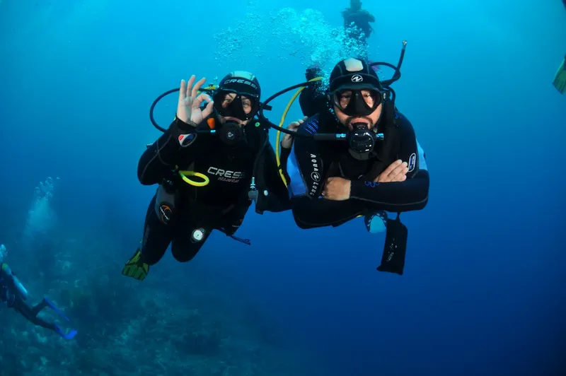 Deux plongeurs en combinaison, souriants, donnent un signe de validation sous l'eau