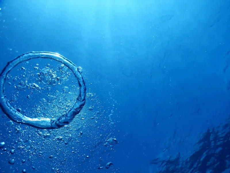 Bulles d'air montant dans l'eau bleue, lumière du soleil filtrée