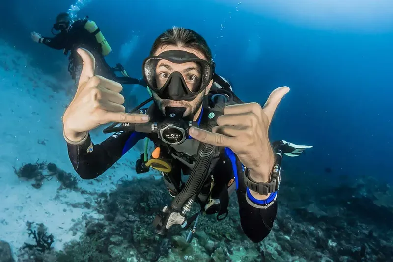 Plongeur souriant fait des signes de pouces levés sous l'eau