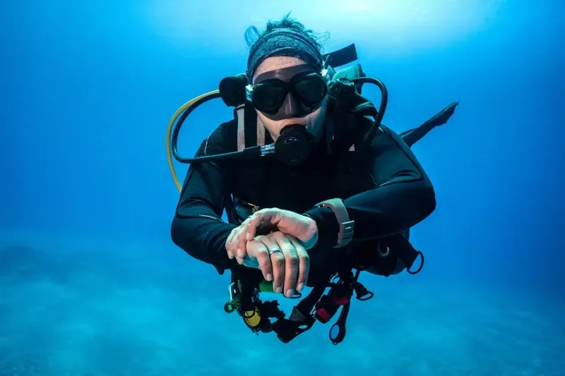 Plongeur en combinaison noire nageant sous l'eau avec un sourire détendu