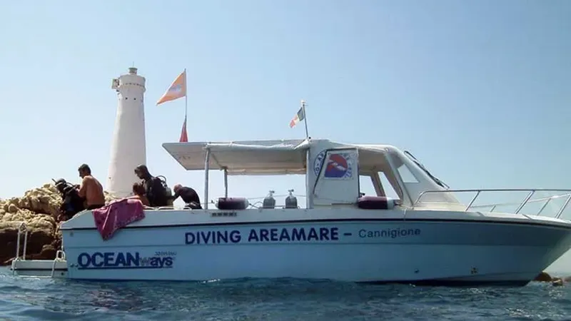 Bateau de plongée avec des plongeurs, phare en arrière-plan, journée ensoleillée