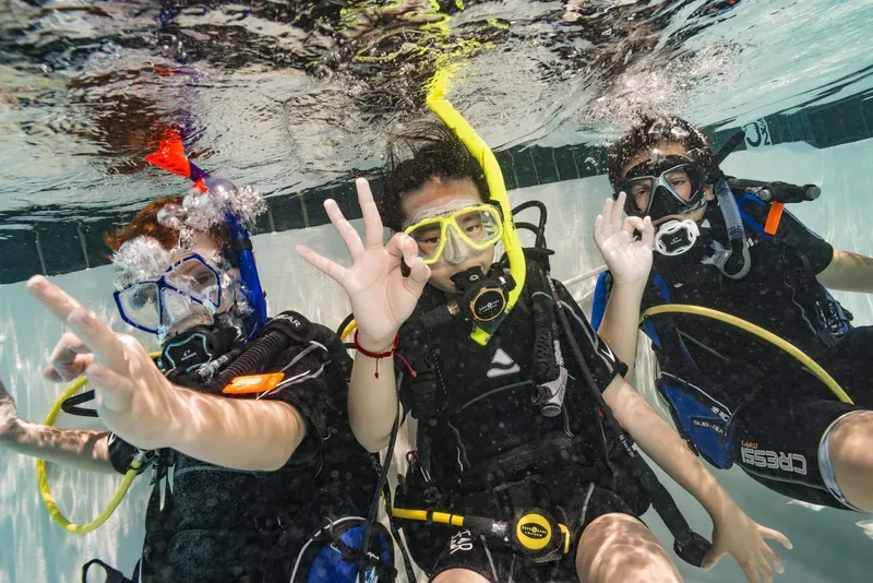 Trois plongeurs souriants font des signes de la main sous l'eau
