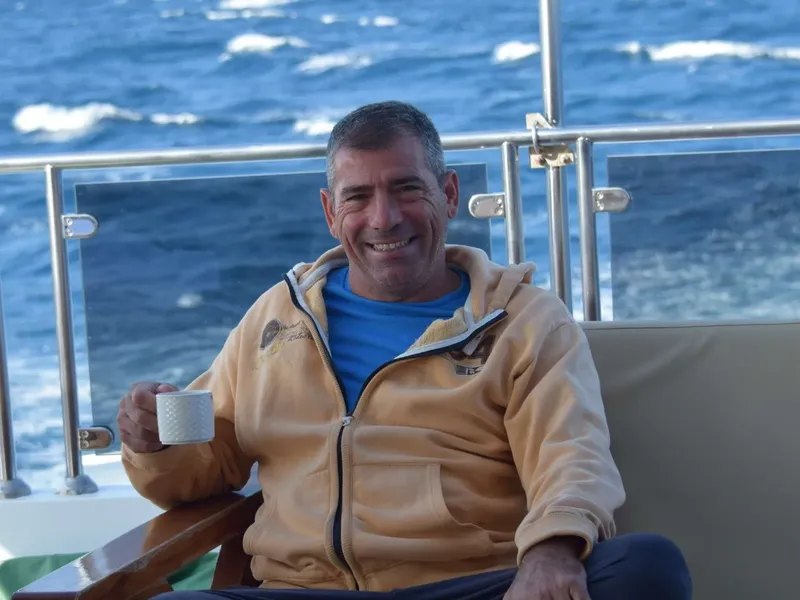 Homme souriant sur un bateau, tenant une tasse blanche