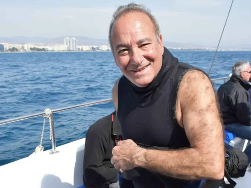 Homme souriant sur un bateau en mer, paysage côtier en arrière-plan