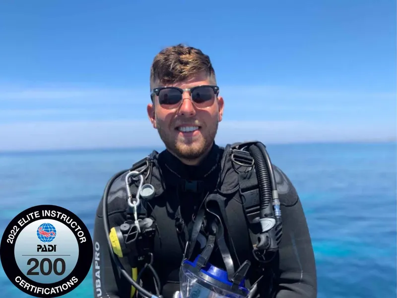 Plongeur souriant avec équipement, portant un badge de certification PADI