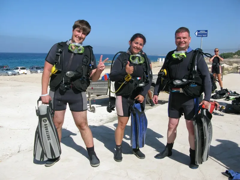 Trois plongeurs souriants équipés sur une plage ensoleillée