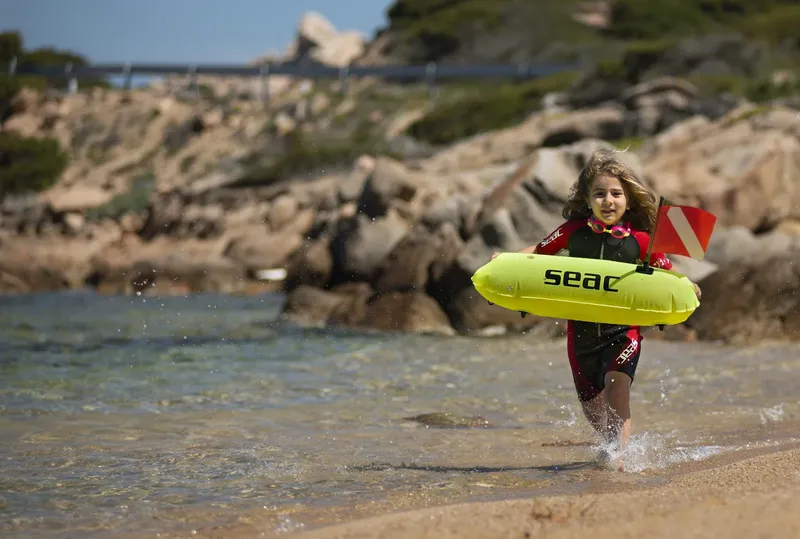 Jeune plongeuse courant sur la plage avec son bouée de signalisation