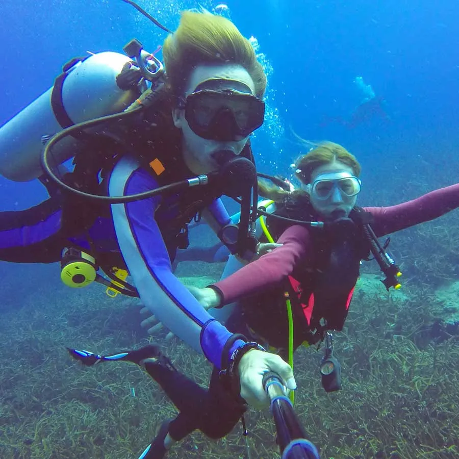 Deux plongeuses souriantes interagissent sous l'eau avec leur équipement
