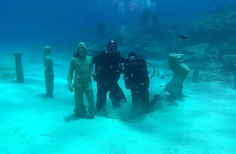Deux plongeurs posent entre des statues sous-marines dans un fond sableux
