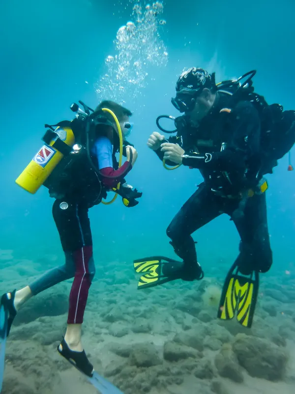 Deux plongeurs en combinaison discutent sous l'eau dans une eau turquoise
