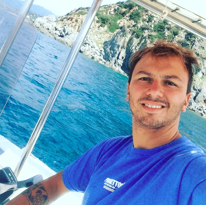Jeune homme souriant sur un bateau en mer, paysage côtier