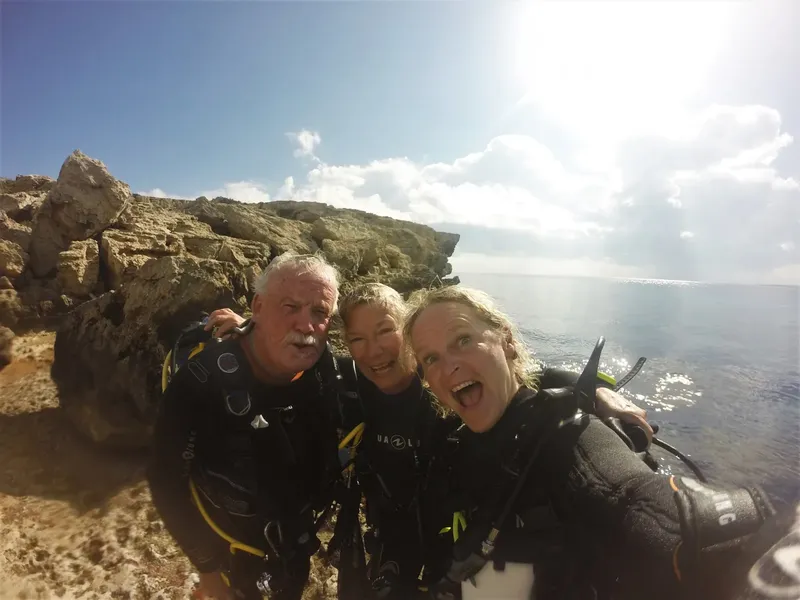 Trois plongeurs souriants posent sur des rochers au bord de la mer