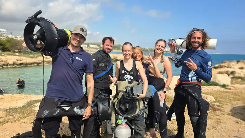 Groupe de plongeurs souriants avec équipement sur une plage rocheuse