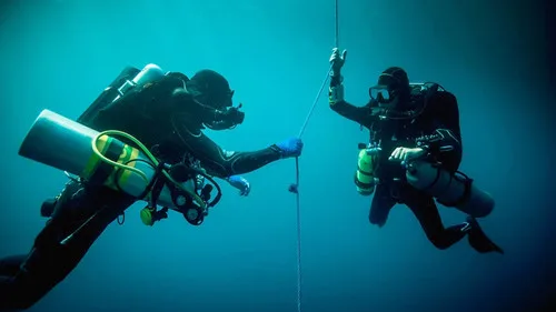 Deux plongeurs en combinaison s'entraident sous l'eau avec une corde