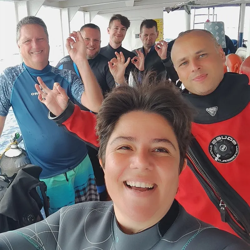 Groupe de plongeurs souriants à bord d'un bateau, signe OK