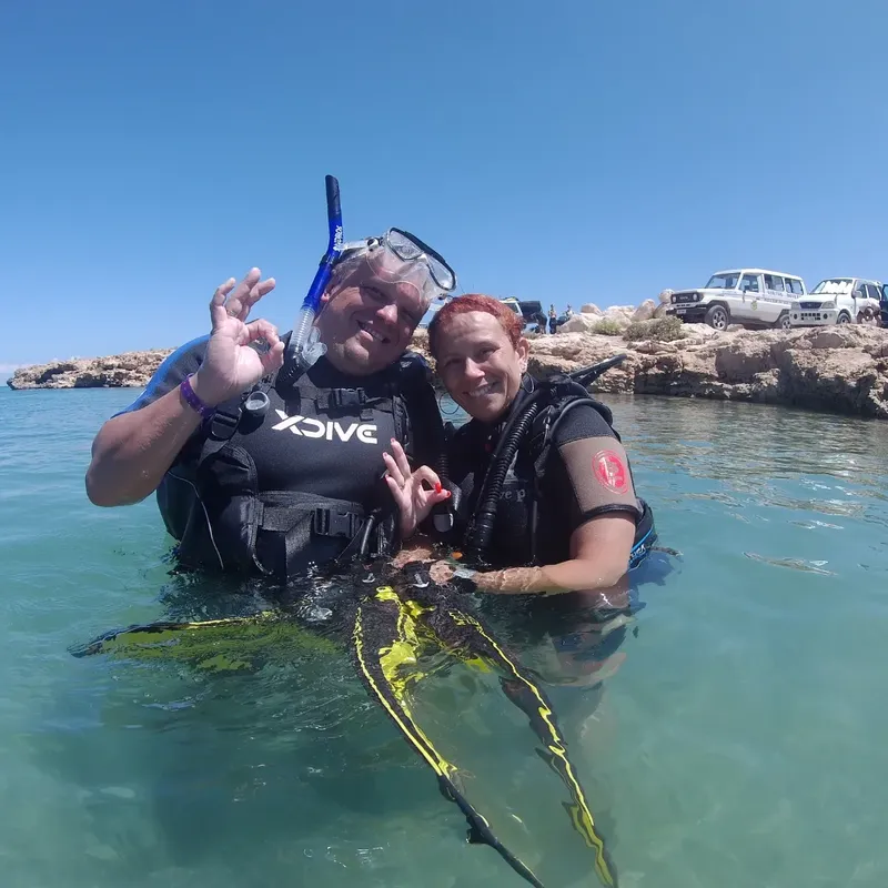 Deux plongeurs souriants dans l'eau claire avec équipement de plongée