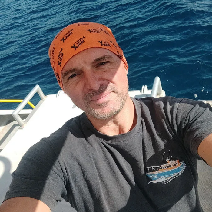 Homme souriant sur un bateau en mer, portant un bandeau et un tee-shirt