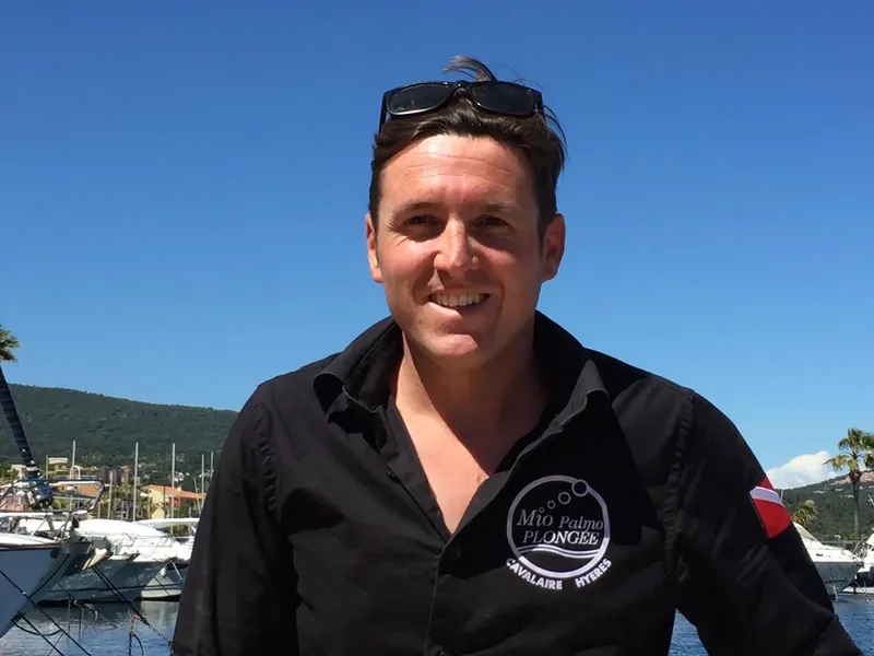 Homme souriant avec lunettes de soleil devant des bateaux et la mer
