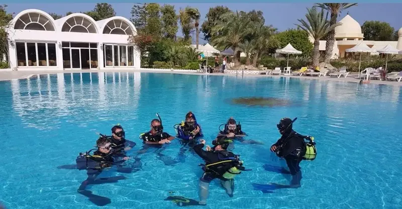 Groupe de plongeurs en formation dans une piscine avec bâtiment blanc